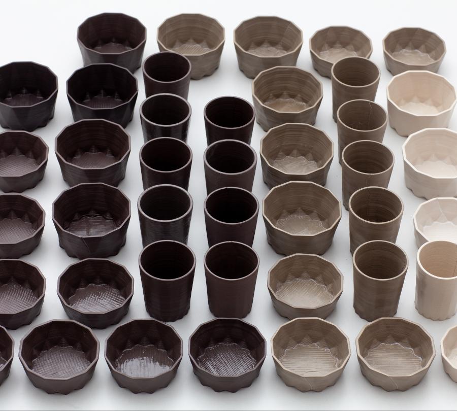 A series of geometrical 3D-printed bowls and glasses, in different earth tones ranging from chocolate brown to bone white.