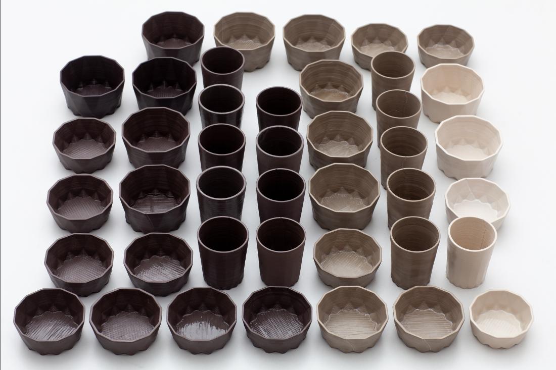 A series of geometrical 3D-printed bowls and glasses, in different earth tones ranging from chocolate brown to bone white.