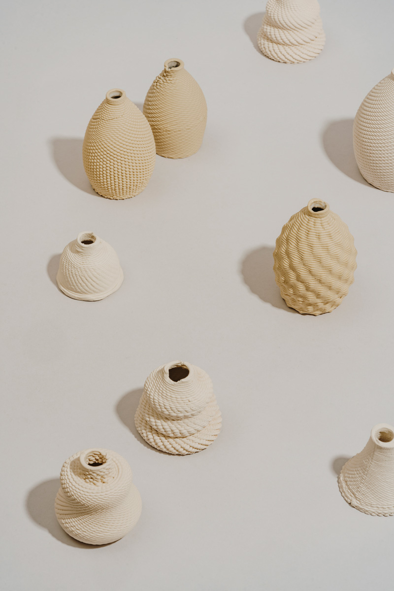 A series of dispersed clay 3D-prints, in the shape of small vases with different textures.