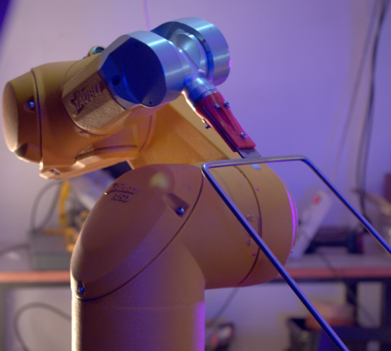 A bright yellow, industrial robotic arm with a metal arc tool attached to its end.